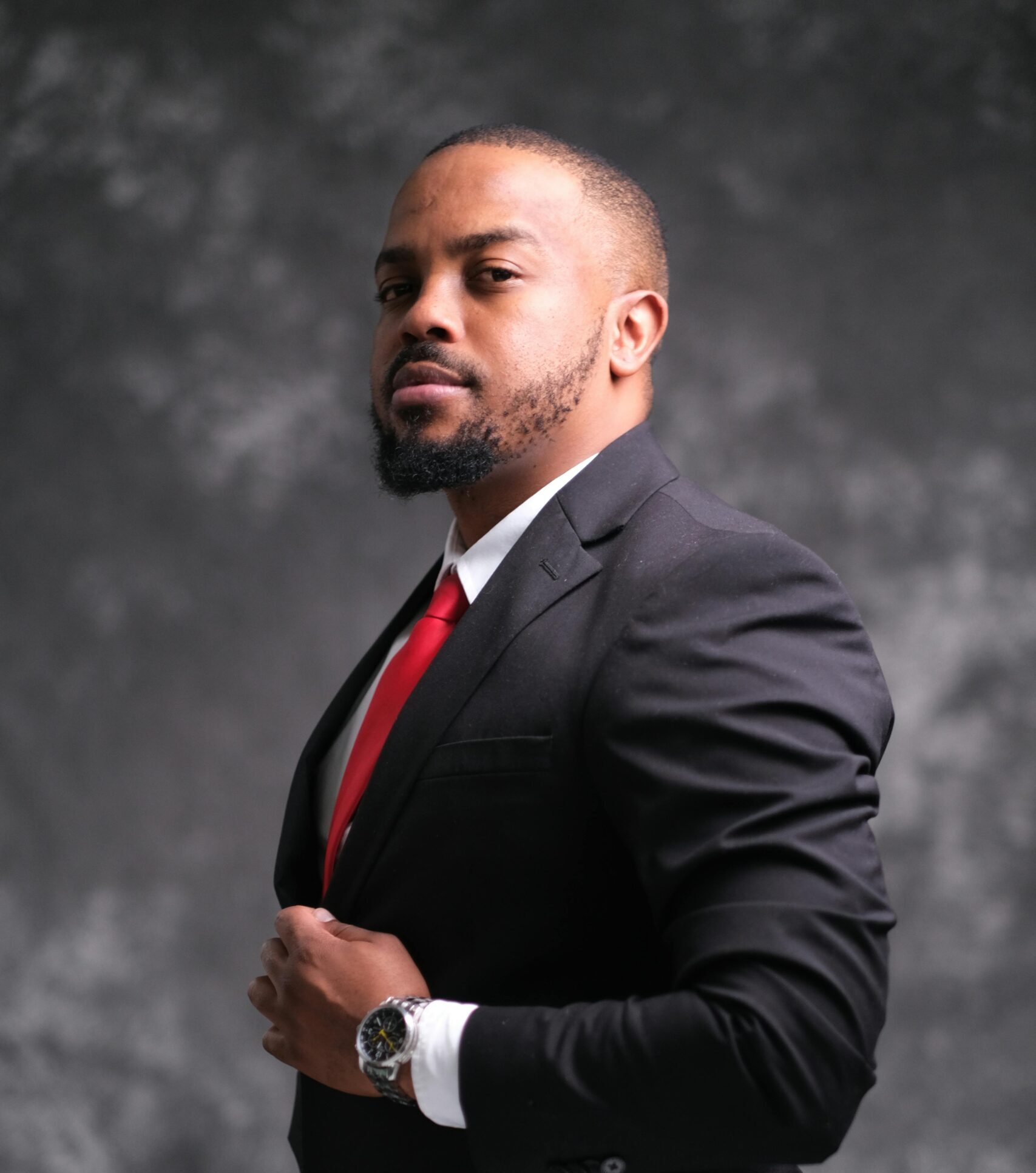 Portrait of a confident man wearing a black suit and red tie, looking assertive.